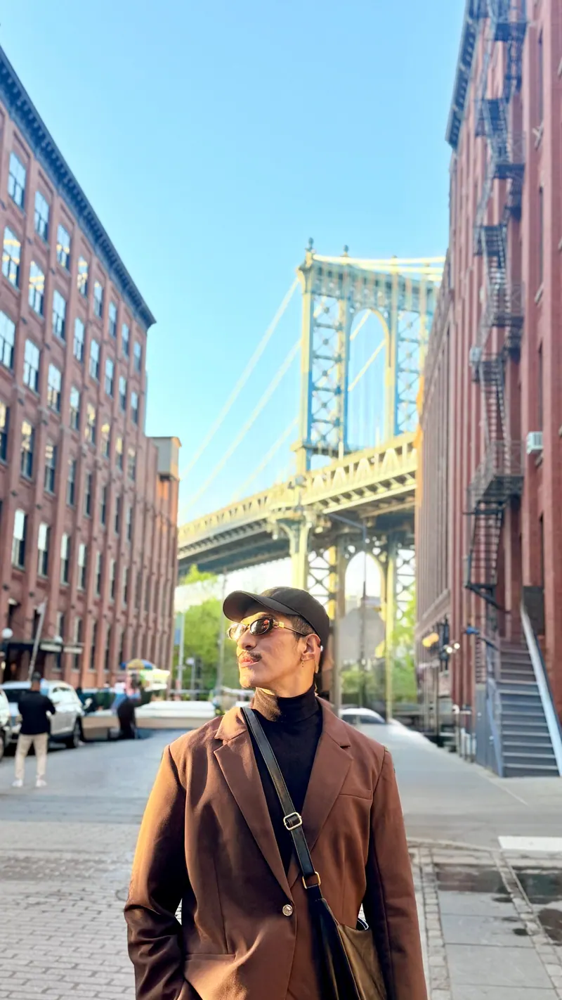 Ives em Dumbo, Nova York, de casaco marrom, com a Manhattan Bridge ao fundo