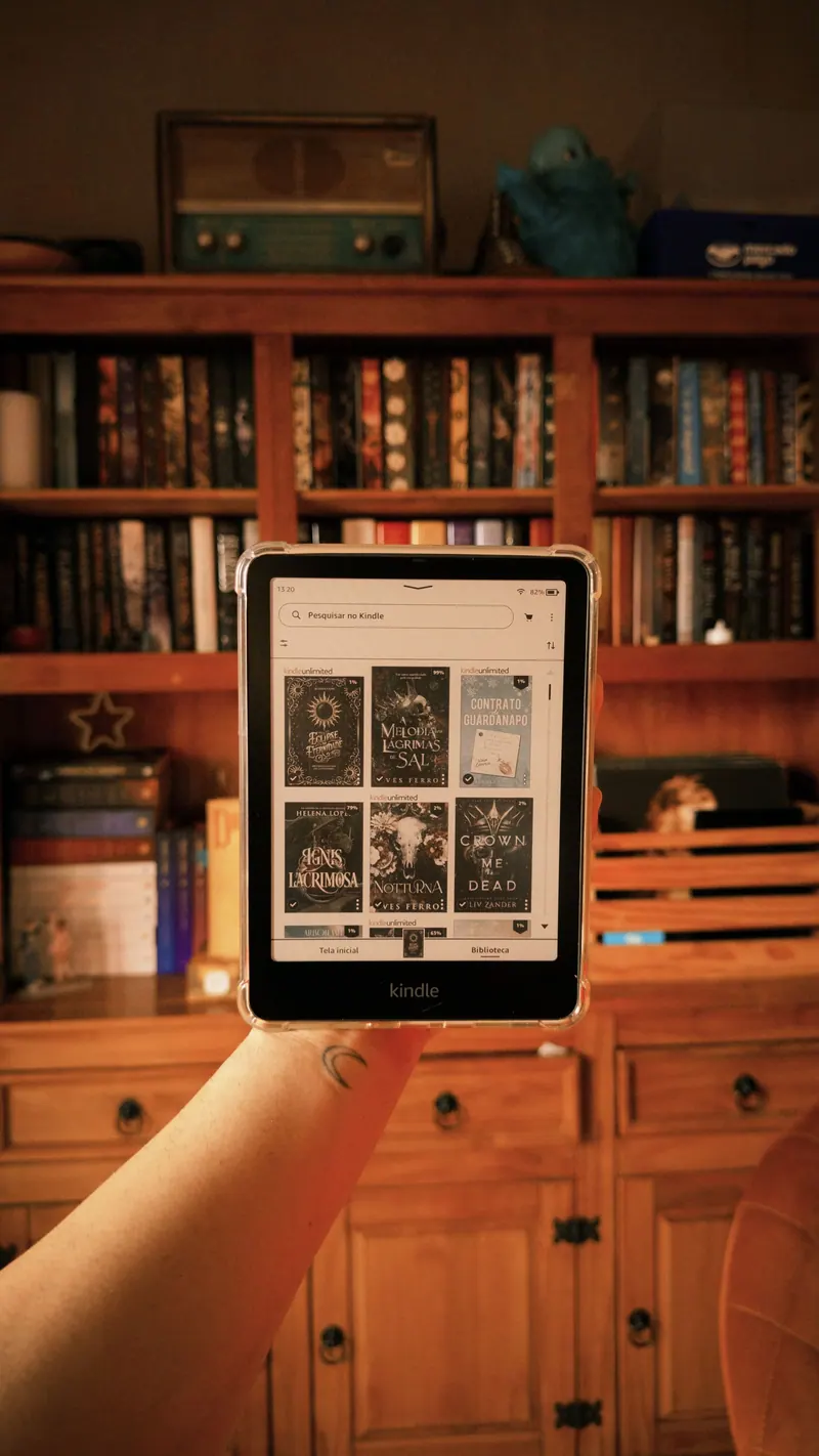 Kindle na mão em frente a uma estante de livros
